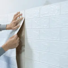 Man applying white brick wallpaper to a wall, covering up mold. Una solución para problemas de humedad.