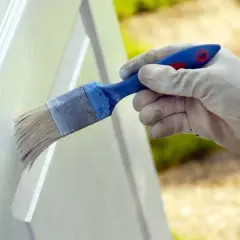 Mano enguantada aplicando pintura blanca a una puerta con brocha. Proceso de lacar puertas en blanco para renovar su aspecto.