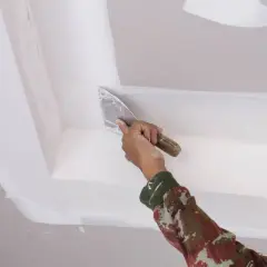 Mano con espátula aplica masilla para reparar techo escayola.