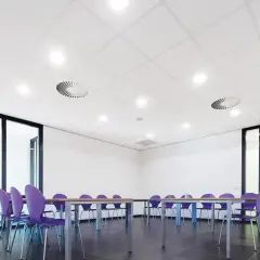 Sala de reuniones con sillas moradas y mesa. El falso techo blanco con luces empotradas y rejillas de ventilación crea un ambiente moderno.