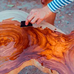 Mano aplica aceite de linaza a una mesa de madera rústica, resaltando sus vetas naturales.