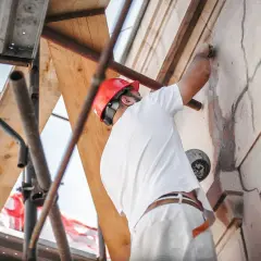 Trabajador con casco rojo repara grietas en fachada, cumpliendo la ley de propiedad horizontal.