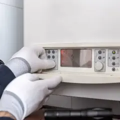 Man con guantes ajusta el panel de control de un calentador estanco, mostrando su pantalla digital y manómetro.