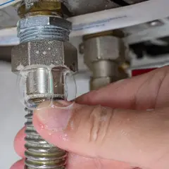 Una mano toca burbujas de agua en una conexión de tubería. Una caldera pierde agua, es peligroso.