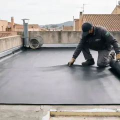 Un trabajador instala una membrana impermeable en una terraza no transitable. El rollo de material negro se desenrolla sobre la superficie.