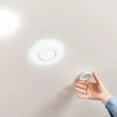Instalando focos empotrados sin falso techo. Mano colocando una luminaria circular en un techo liso.