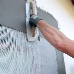 Obrero aplica mortero sobre malla de refuerzo para asegurar la durabilidad de la fachada.