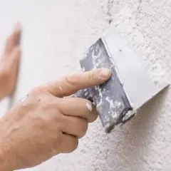 Mano aplicando masa para reparar gotele en una pared texturizada.