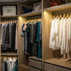 Armario con ropa colgada y cajas de almacenamiento. La iluminación del vestidor resalta la organización y el estilo.