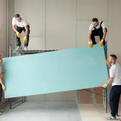 Cuatro obreros instalan un gran panel de pladur para crear un tabique con puerta.