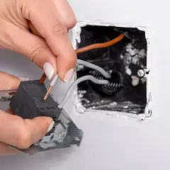 Manos conectando cables a un interruptor conmutador dentro de una caja empotrada en la pared.