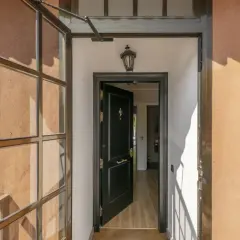 Puerta principal negra abierta, con ventana lateral y luz de porche. Ideas para cerrar un porche con estilo moderno.