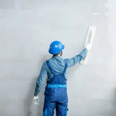 Obrero con casco azul alisa una pared con imperfecciones usando una llana.