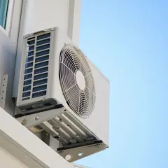 Unidad exterior de aire acondicionado montada en pared blanca, ideal para saber donde colocar la unidad exterior del aire acondicionado para una ventilación óptima.