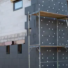 Fachada de edificio en construcción con aislamiento de poliestireno expandido gris, conocido como llana mineral, y andamios.