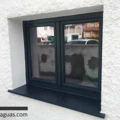 Ventana con marco oscuro y alféizar negro, lista para rematar ventanas por fuera. Refleja una calle con casas y coches.