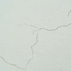 Detalle de grietas finas en una fachada de color crema, mostrando el paso del tiempo y la textura del material.