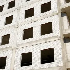 Fachada monocapa blanco de edificio en construcción, con ventanas vacías y balcones de hormigón.