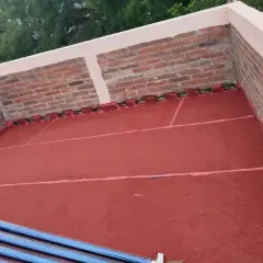 Terraza con pintura impermeabilizante roja recién aplicada. Se aprecian ladrillos y tubos de calentador solar.