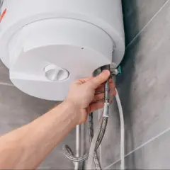 Mano conectando mangueras a un termo eléctrico. Guía para saber como vaciar un termo eléctrico de forma segura.