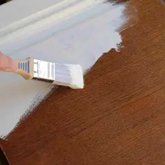 Mano pintando una puerta de madera con brocha blanca. El proceso de pintar puertas de madera es un proyecto de bricolaje común.