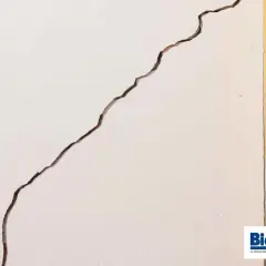 Grieta profunda en pared blanca, junto a marco amarillo y puerta de madera. Guía para saber como arreglar grietas profundas en paredes.