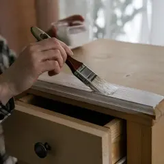 Persona aplicando pintura blanca a un armario de madera con un pincel. Paso a paso como pintar un armario de madera.