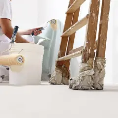 Pintor prepara cubos con rodillos para pintar. Se aprecian distintos tipos de rodillos para pintar, una escalera y cubos de pintura.