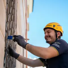 Hombre con casco amarillo sonríe mientras realiza el revoco de paredes con una brocha azul.