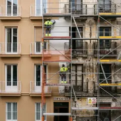 Trabajadores en andamios rehabilitan fachadas de edificios en una calle urbana.