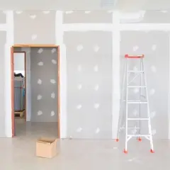 Habitación en construcción con paredes de enfoscado de yeso, una escalera y una caja de cartón.