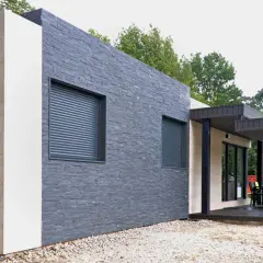 Muros exteriores de casas modernas con texturas de piedra y acabados claros. Ventanas con persianas enrollables y un porche con mobiliario.
