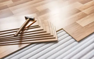 Tablas de suelo laminado apiladas con martillo y lápiz, listas para instalar sobre una base que protege de la humedad que sube del suelo.