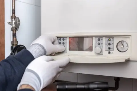 Man con guantes ajusta el panel de control de un calentador estanco, mostrando su pantalla digital y manómetro.
