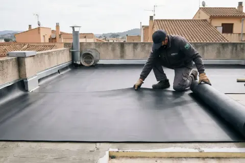 Un trabajador instala una membrana impermeable en una terraza no transitable. El rollo de material negro se desenrolla sobre la superficie.