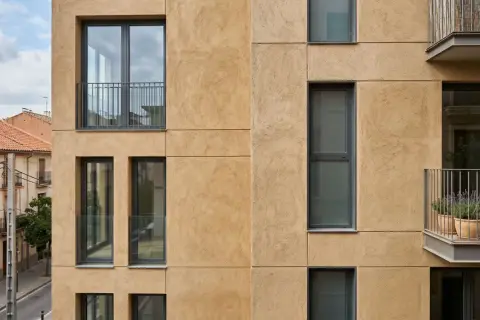 Fachada moderna con acabado de mortero para reparación, ventanas rectangulares y balcones con barandillas metálicas.