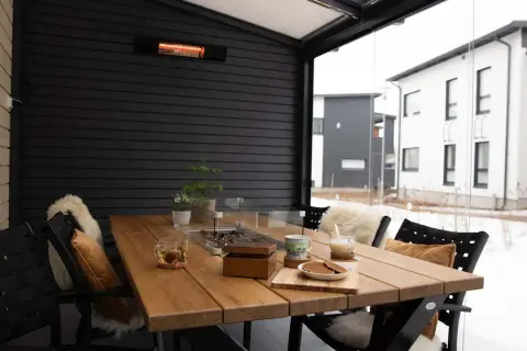 Mesa de madera en terraza cerrada con calefactor, ideal para disfrutar de una bebida caliente en invierno.