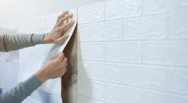 Man applying white brick wallpaper to a wall, covering up mold. Una solución para problemas de humedad.