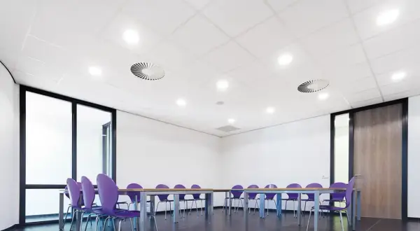 Sala de reuniones con sillas moradas y mesa. El falso techo blanco con luces empotradas y rejillas de ventilación crea un ambiente moderno.