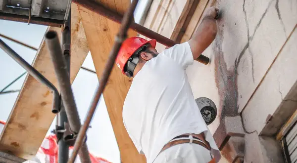 Trabajador con casco rojo repara grietas en fachada, cumpliendo la ley de propiedad horizontal.