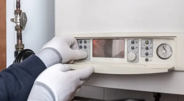 Man con guantes ajusta el panel de control de un calentador estanco, mostrando su pantalla digital y manómetro.