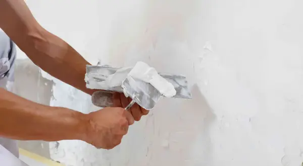 Man applying enfoscado de mortero a una pared con una llana.