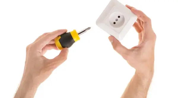 Manos sujetan destornillador y enchufe, listos para aprender como poner un enchufe en un cable.