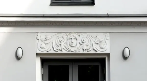 Detalle arquitectónico: una cornisa con un rostro femenino y volutas decorativas sobre una puerta.