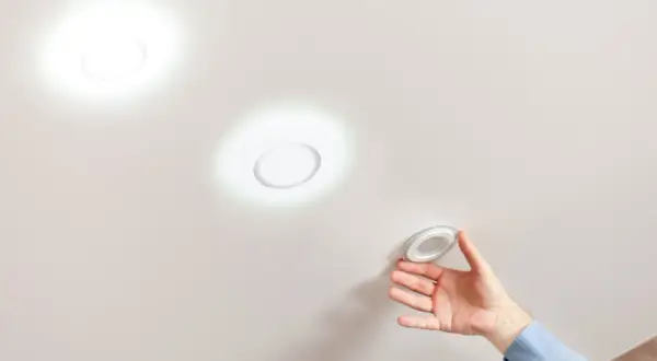 Instalando focos empotrados sin falso techo. Mano colocando una luminaria circular en un techo liso.