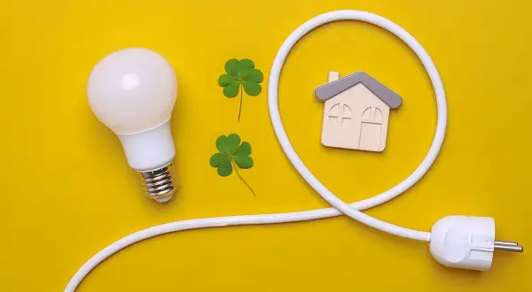 Bombilla, tréboles y un enchufe con forma de casa simbolizan el confort visual y la energía en el hogar.