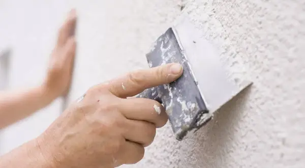 Mano aplicando masa para reparar gotele en una pared texturizada.