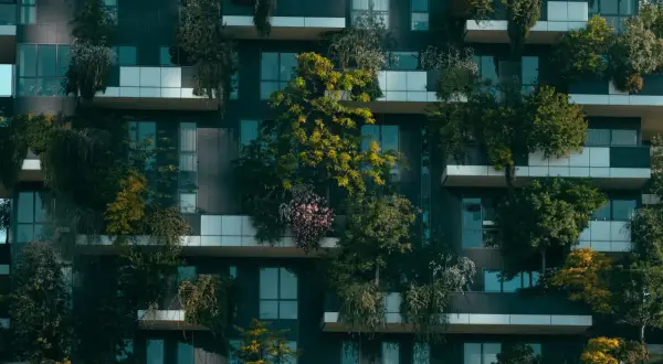 Edificio moderno con balcones repletos de vegetación, un ejemplo de sostenibilidad en la construcción que integra la naturaleza en la vida urbana.