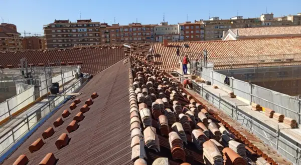 Trabajadores en un tejado, reemplazando tejas como parte de la rehabilitación de edificios antiguos.
