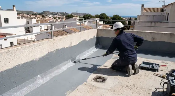 Persona impermeabiliza terraza con rodillo, aplicando pintura gris sobre malla de refuerzo.